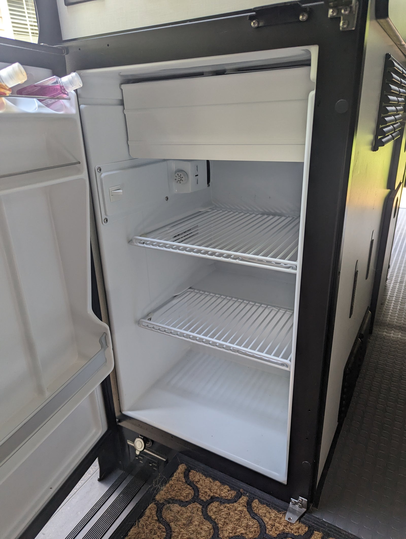 RV rental appliance: Open, clean mini-fridge with wire shelves, a small freezer, and two bottles inside.