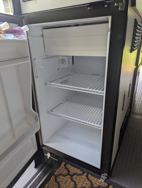 RV rental appliance: Open, clean mini-fridge with wire shelves, a small freezer, and two bottles inside.