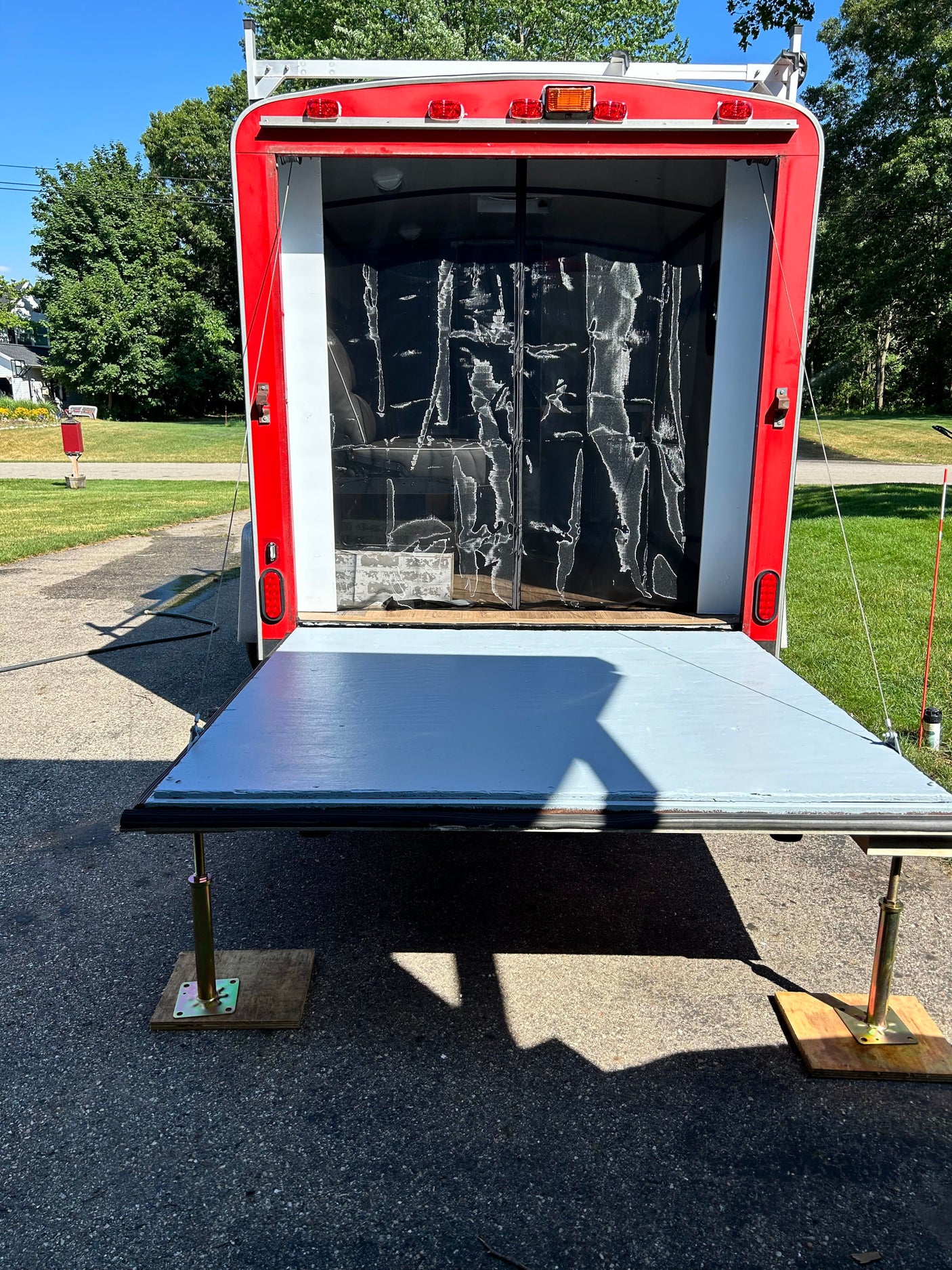 Rear of a red/white utility trailer with its ramp lowered, supported by posts. Ready for gear, perfect for RV rental adventures.