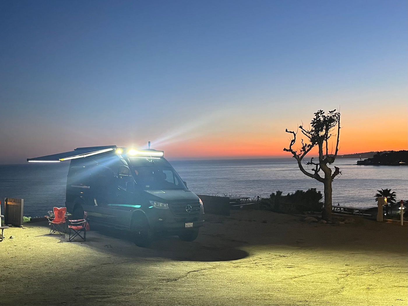 Overland Mercedes Sprinter RV rental parked oceanside at dusk, lights illuminating the camp area. — photo 15