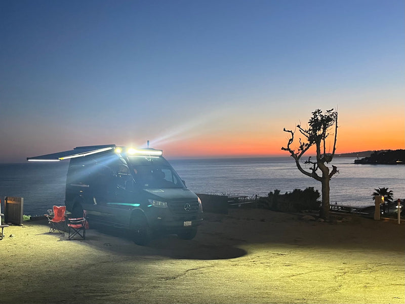 Overland Mercedes Sprinter RV rental parked oceanside at dusk, lights illuminating the camp area. — photo 15