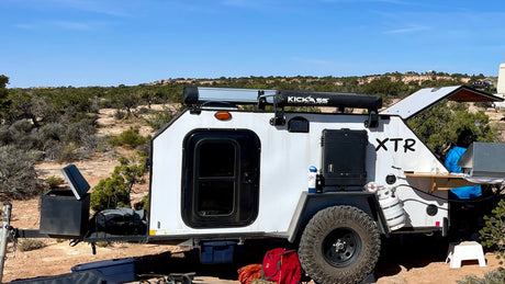 An XTR off-road teardrop trailer, ideal for an RV rental, is set up for camping in a rugged desert environment.