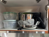 RV rental kitchen: stacked plastic food containers, metal bowls with felt protectors for compact cabinet storage.
