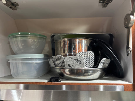 RV rental kitchen: stacked plastic food containers, metal bowls with felt protectors for compact cabinet storage.
