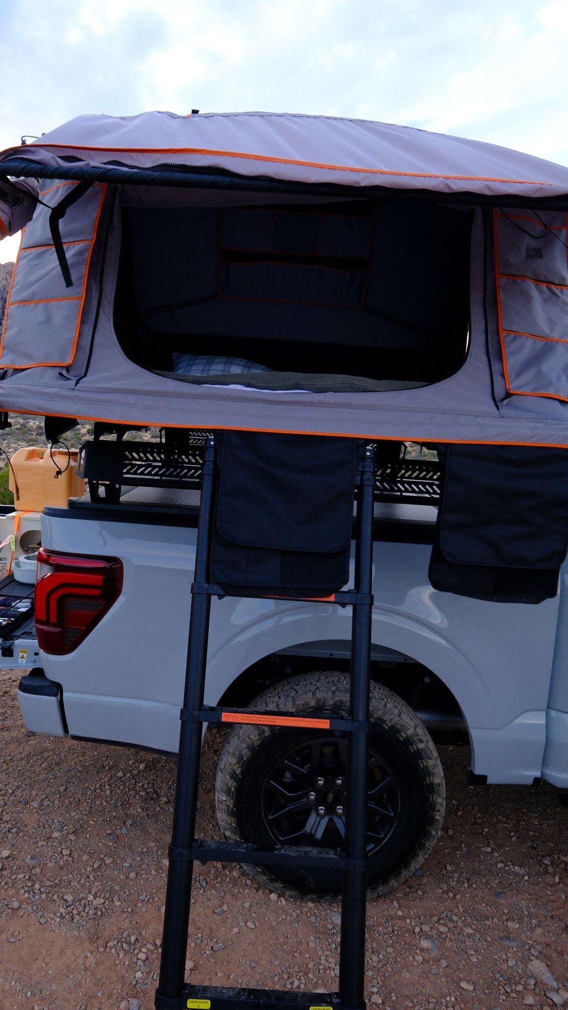 Experience overlanding with this rv rental truck & rooftop tent setup. Features ladder, cozy bedding, & storage pockets. — photo 13