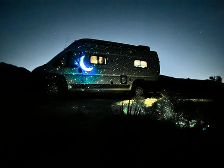 An RV glows with projected stars and a crescent moon under a dark night sky. Imagine this peaceful rv rental experience.