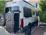 White Revel 4x4 Sprinter van, great for an RV rental. Features a rear ladder, spare tire, and large black gear box.