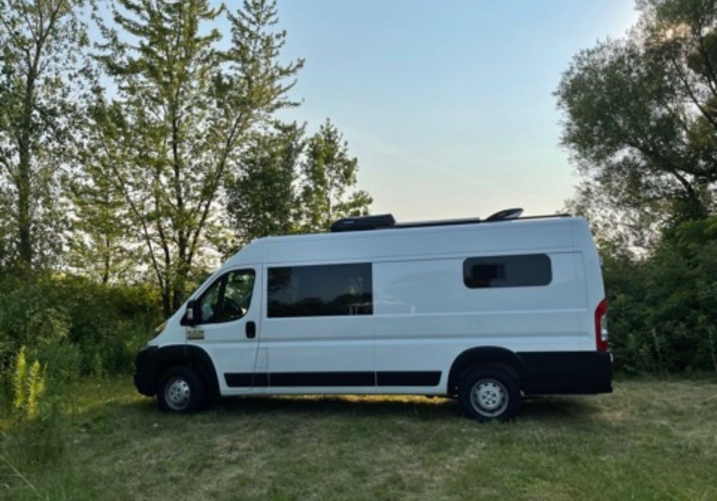A sleek white camper van RV rental is parked on a grassy patch amidst green trees — photo 1