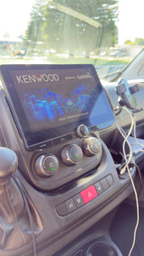RV rental dashboard with Kenwood/Garmin navigation screen and climate controls, visible under bright sunlight.