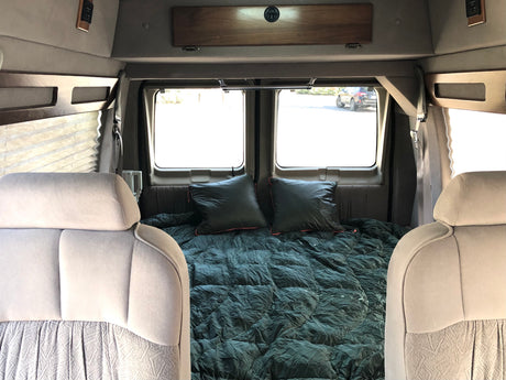 Step inside this cozy RV rental's camper van interior, featuring a comfortable bed, pillows, and bright windows for mobile travel.