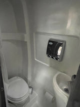 This RV rental features a compact bathroom with a white toilet, small sink, and wall-mounted chrome dispenser.