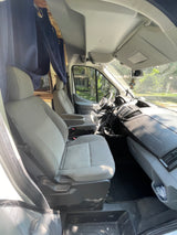 Inside an RV rental van: driver & passenger seats, dashboard, & steering wheel. Blue curtains separate the front cabin from the living area.