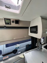Inside an RV rental: Controls for heating and systems, a compact kitchen with sink, and window showing another vehicle, offering comfort for travel.