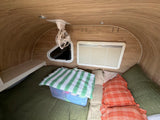 Comfortable rv rental interior: bed with green & orange pillows, ceiling fan, and window with blinds for a cozy sleep.