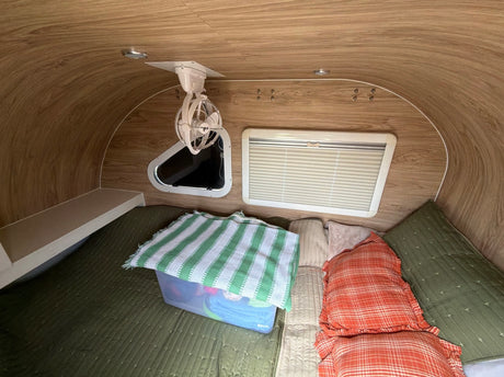 Comfortable rv rental interior: bed with green & orange pillows, ceiling fan, and window with blinds for a cozy sleep.