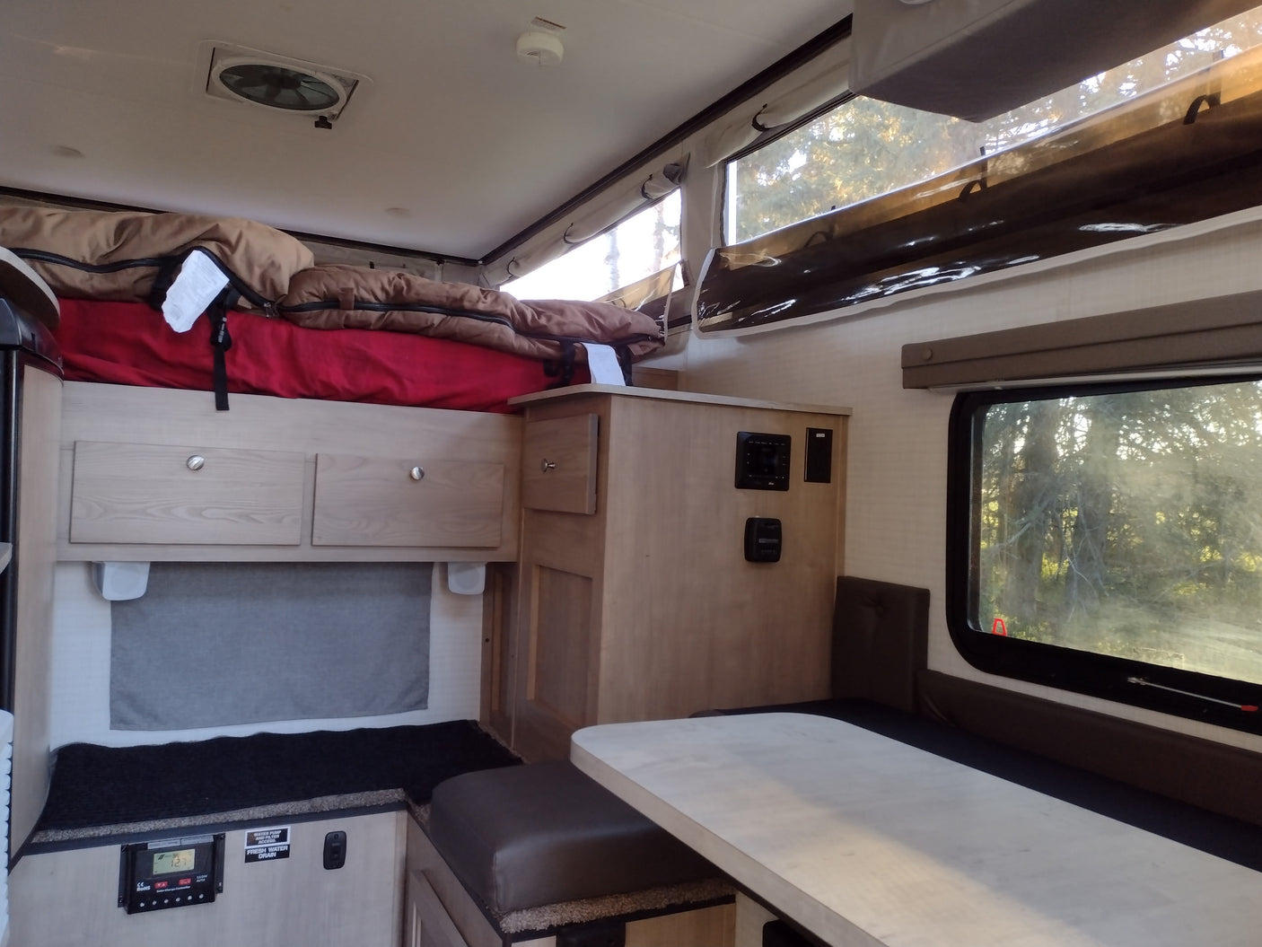 Cozy RV rental interior with elevated bed, dinette, and control panel for comfortable travels.