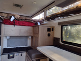 Cozy RV rental interior with elevated bed, dinette, and control panel for comfortable travels.