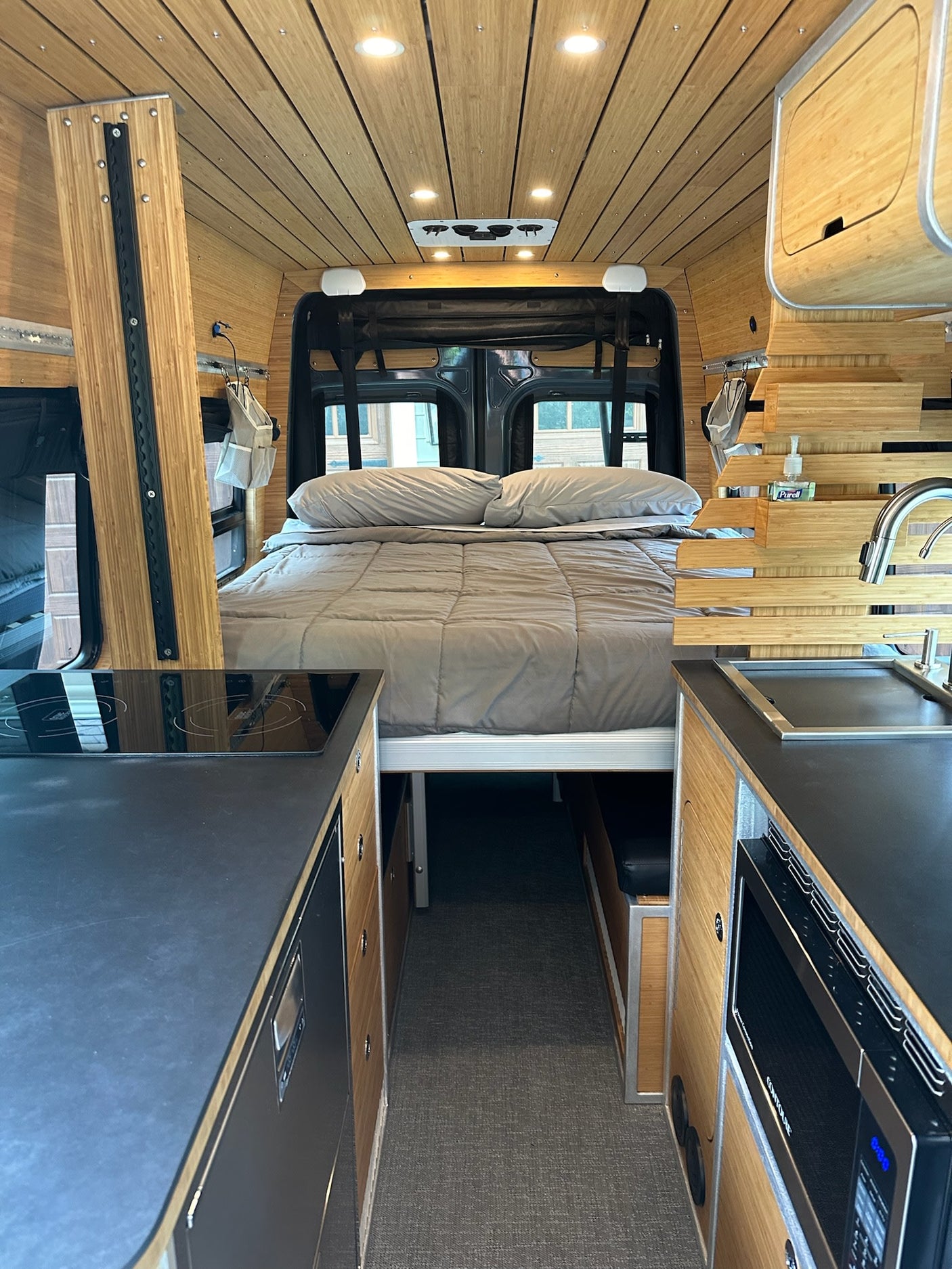 Modern rv rental interior: A stylish camper van featuring a comfortable bed, induction cooktop, and sink with wood paneling.