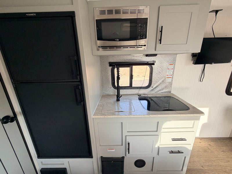 Bright rv rental kitchen: black fridge, microwave, sink, cooktop, and light cabinetry, perfect for small space living. — photo 9