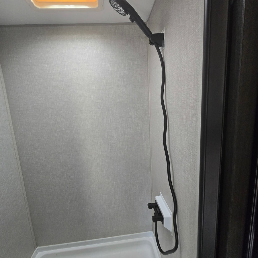 RV rental shower: compact space with light textured walls, white pan, and a black shower head and faucet.
