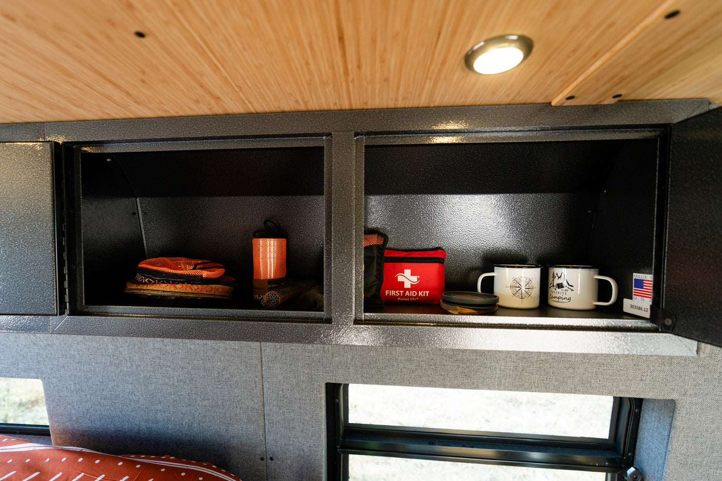 Overhead cabinets in an RV rental, showing camping mugs, a first aid kit, and organized gear for travel.