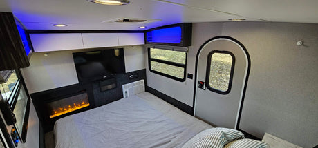 Step inside this cozy RV rental bedroom, complete with a striped bed, TV, electric fireplace, AC, and blue accent lighting.