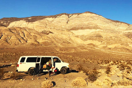 White RV rental in desert, huge mountains backdrop. Relaxing outside, perfect for your next adventure.