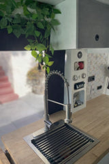 Modern RV rental kitchen features a stylish gooseneck faucet, sink with a drying rack, wood countertop, and a fresh green plant.