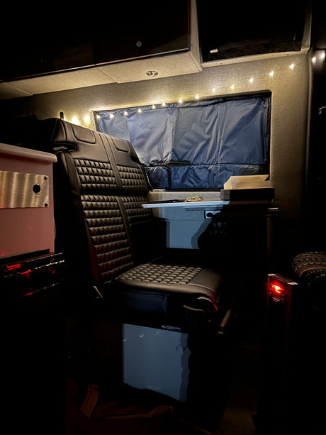 Cozy RV rental interior at night, featuring a quilted black seat, ambient string lights, and window shade.