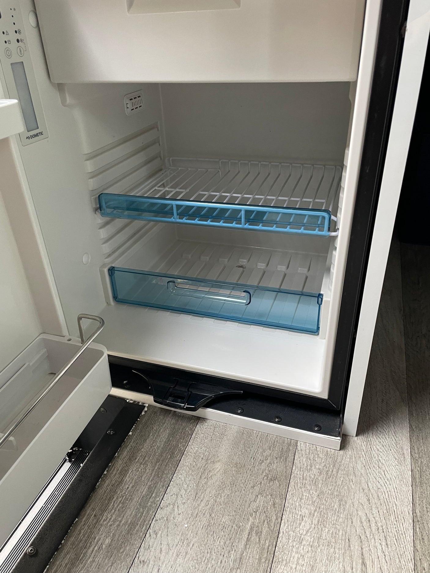 A clean, empty Dometic refrigerator interior, typically found in an RV rental, with shelves and control panel visible. Ready for use.