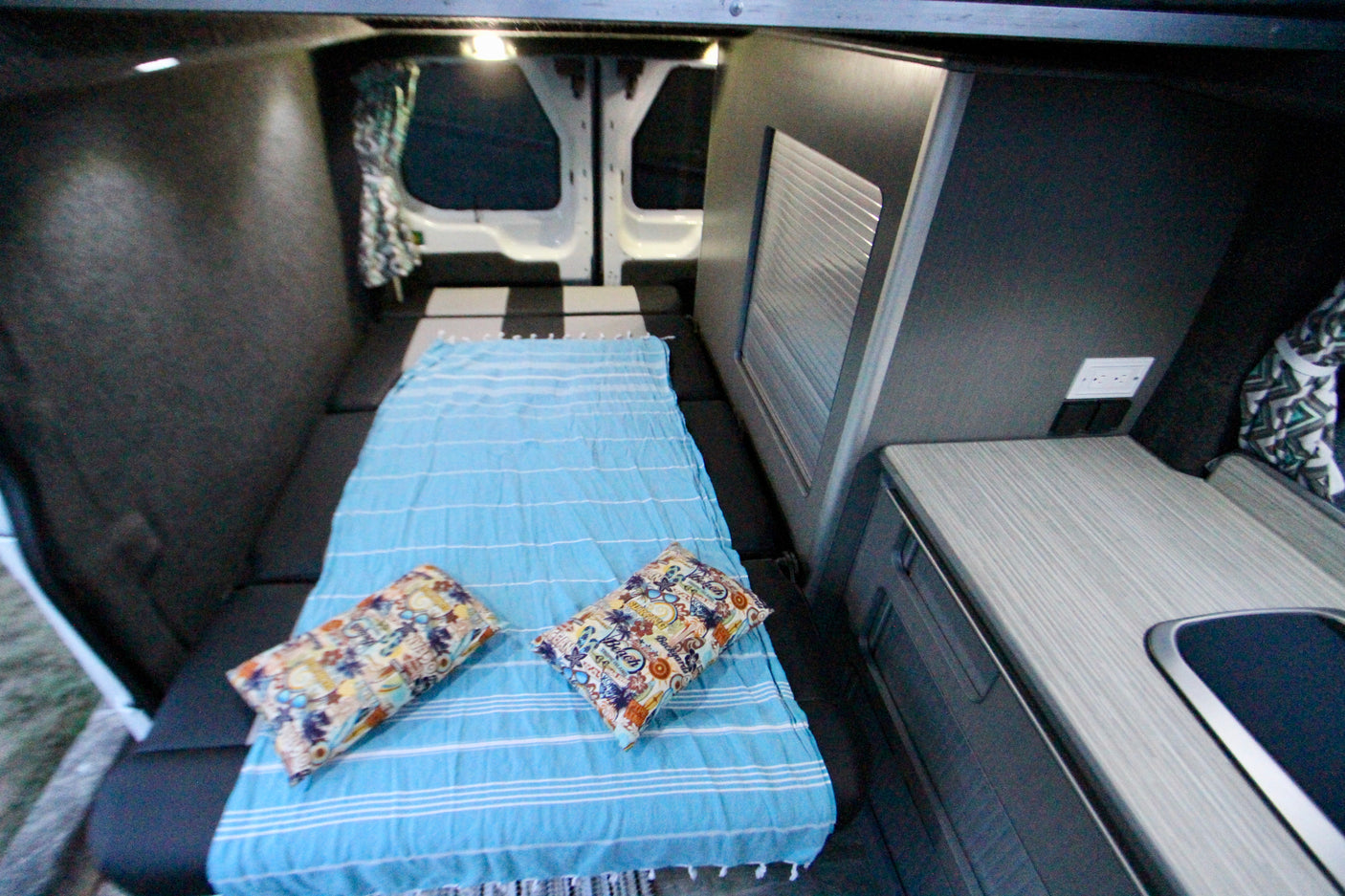 Spacious RV rental interior featuring a comfy bed with blue blanket, colorful pillows, and a compact kitchen counter.