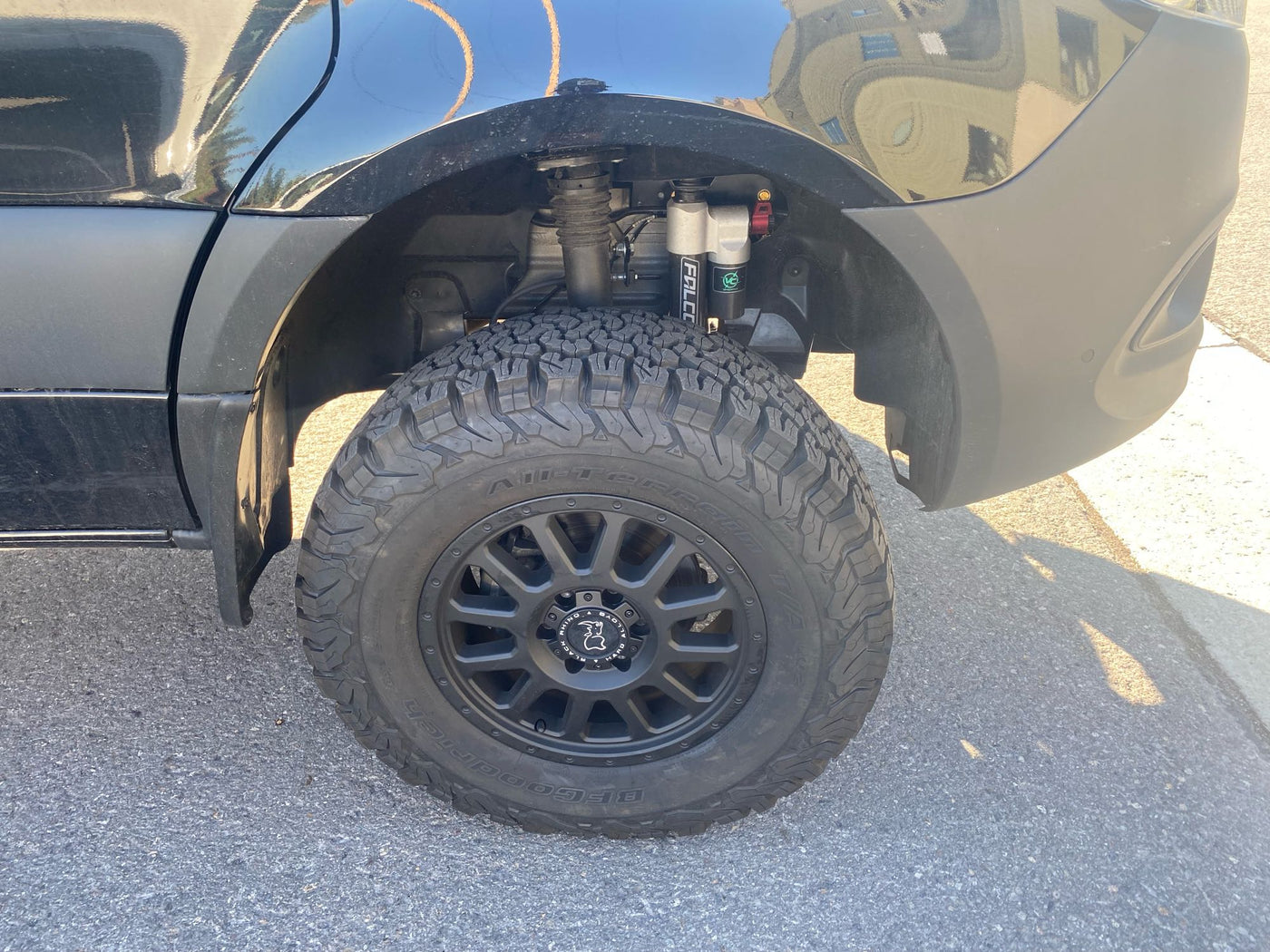 Close-up of a customized black van's rear wheel with rugged tires and Falcon shocks, perfect for your next RV rental adventure. — photo 7