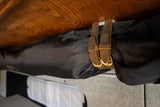 RV rental interior: Leather straps with buckles secure a black storage bag under a wooden surface.