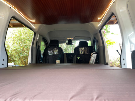 View from the back of an RV rental conversion van, showing a comfortable bed, ceiling LEDs, and front cabin.