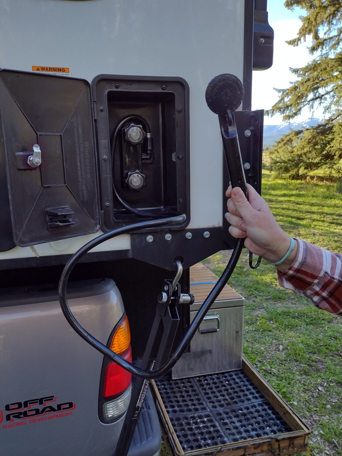 Outdoor shower setup on this RV rental: connections, showerhead in hand, and winterizing instructions visible. Great for camping!