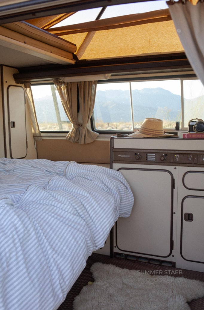  reading a book on a striped bed inside a cozy camper van interior.|Your cozy home on wheels: this RV rental offers a comfortable bed — photo 14