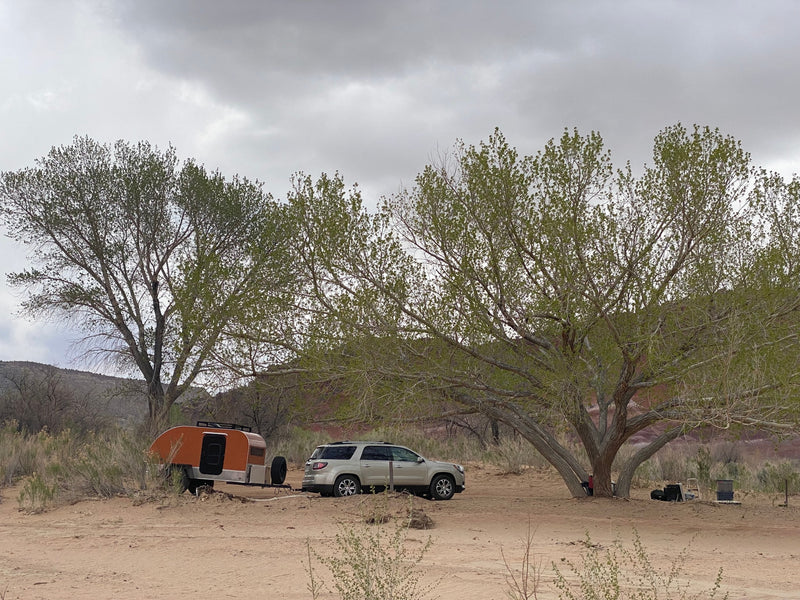An SUV tows an orange teardrop RV rental, parked on sandy terrain under large trees, ideal for outdoor camping. — photo 10