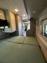 RV rental interior: Comfortable convertible bed, overhead lights, TV, and a view into the cockpit area.