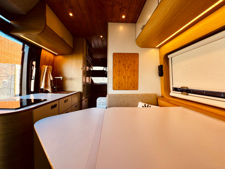 Modern RV rental interior: a sleek wood-paneled camper van featuring a kitchen, dining area, and ambient strip lighting.