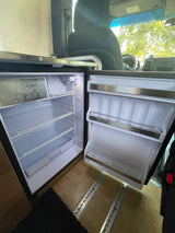 An RV rental's open, empty compact refrigerator with wire shelves and a small freezer. Ready for use!