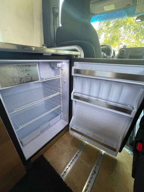 An RV rental's open, empty compact refrigerator with wire shelves and a small freezer. Ready for use!