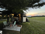 Unwind on your RV rental adventure! This image shows a camper, outdoor seating, and string lights at sunset by a field.