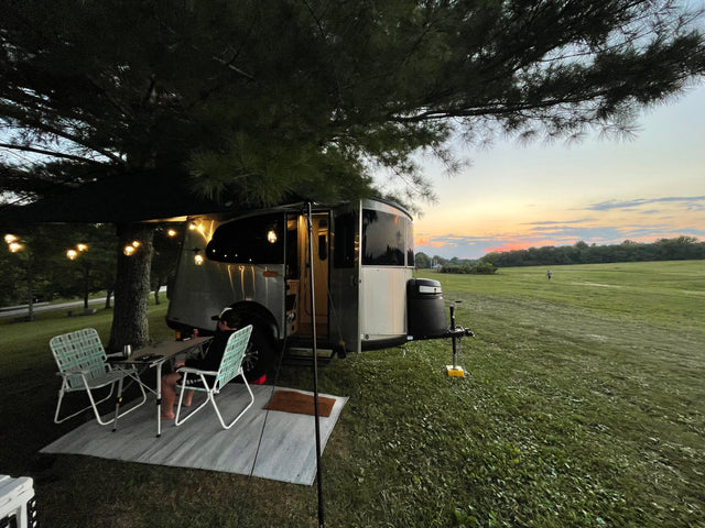 Unwind on your RV rental adventure! This image shows a camper, outdoor seating, and string lights at sunset by a field.