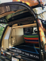 Explore a cozy RV rental camper's customized interior with built-in storage, colorful blanket, and Pink Floyd "Dark Side" blanket.