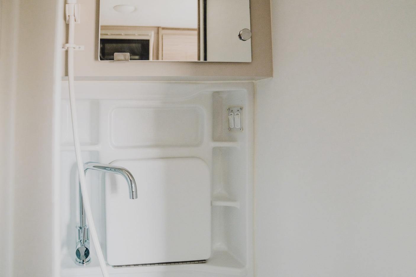 RV rental wet bath: compact space with sink, chrome faucet, mirror, and shower holder. Functional for travel.