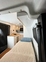 Bright RV rental interior: compact kitchen with wood counter/sink, plus two cozy bed areas visible.