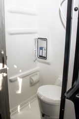 Inside an RV rental: a compact wet bath featuring a toilet, shower, and convenient wall storage with toiletries.
