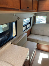 Cozy RV rental interior with light seating, overhead cabinets, and windows showing the outside. Perfect for road trips.