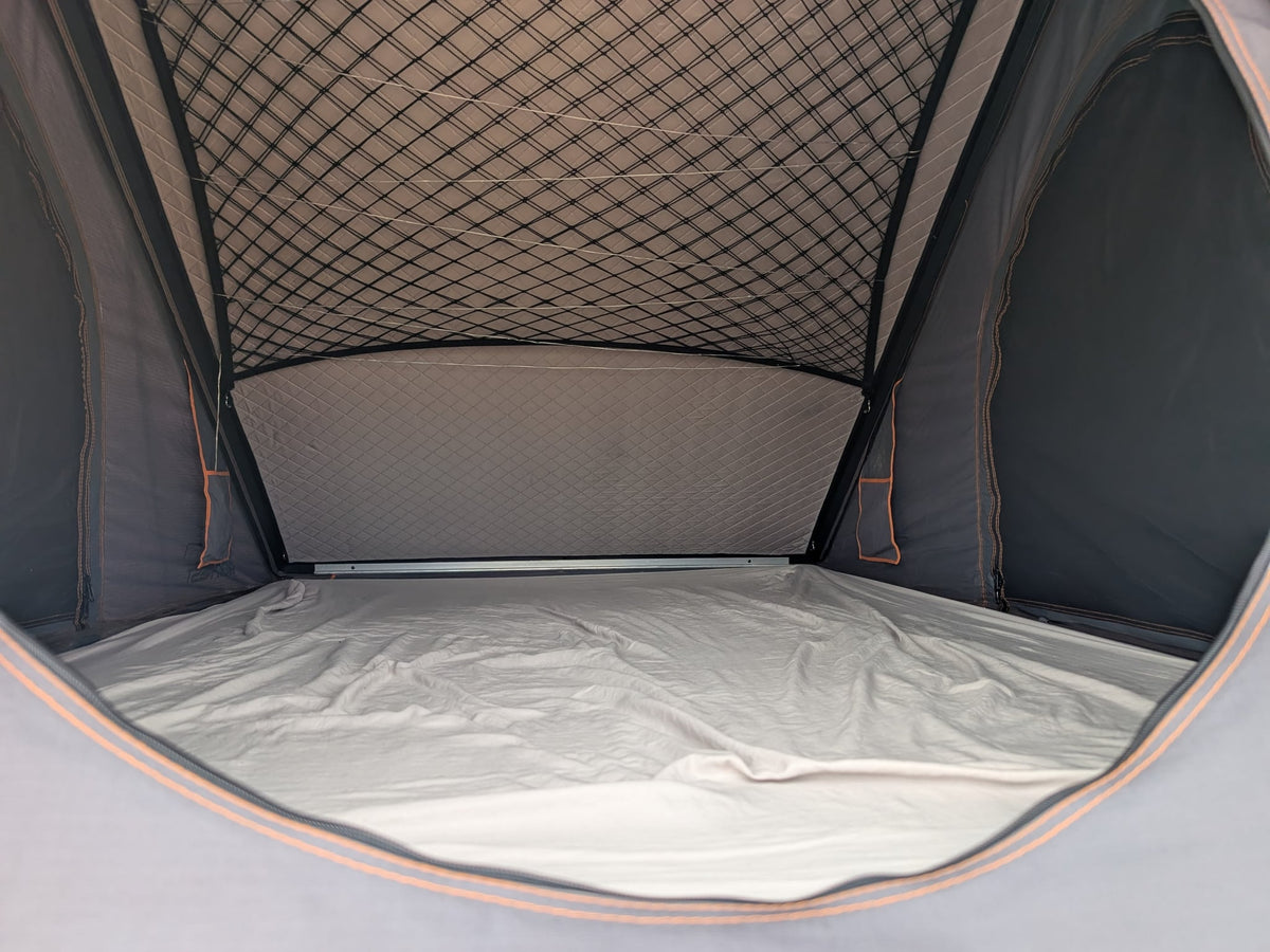  watching cars pass by dry hills and distant mountains.|Cozy RV rental rooftop tent interior. Features a comfortable sleeping area with a mattress — photo 4