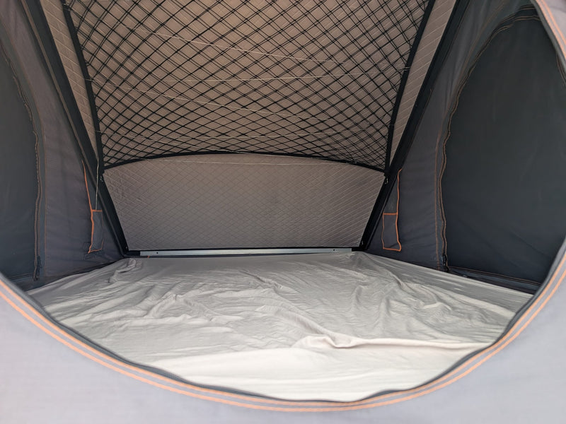  watching cars pass by dry hills and distant mountains.|Cozy RV rental rooftop tent interior. Features a comfortable sleeping area with a mattress — photo 4